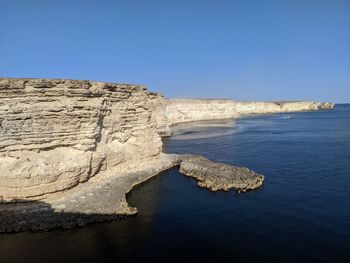 Rock formations by sea against clear blue sky