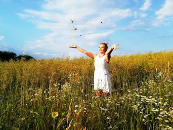 Woman with arms raised standing on field against sky