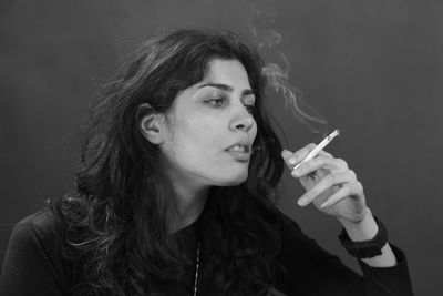 Sad woman smoking cigarette against gray background
