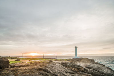 Lighthouse by sea against sky during sunset