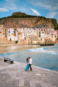 Friends on the beach by buildings against sky