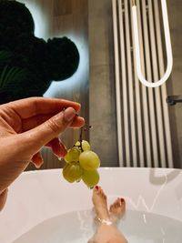 Hand holding grape in bath against feet