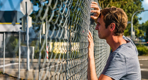 Caucasian man leaning forehead against outdoor fence deep in thought. profile view.