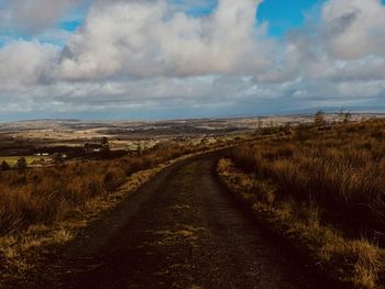 Dirt road amidst field against sky