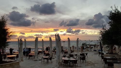 Chairs and tables at beach against sky during sunset