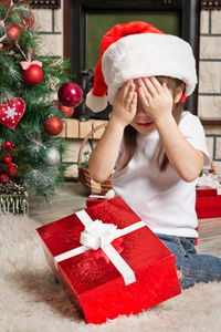 Cute girl covering eyes with hands while sitting at home