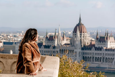 Young woman on balcony overlooking hungarian parliament in budapest, hungary