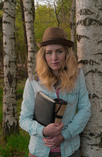 Portrait of beautiful woman standing by tree trunk in forest