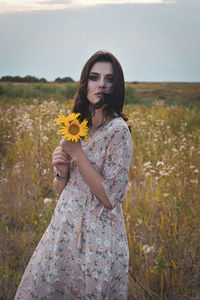 Woman standing by flower on field against sky