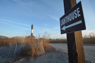 Sign on wooden post by road against sky during winter
