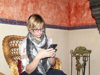 Mid adult woman using phone while sitting on chair at home