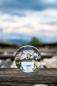 Close-up of crystal ball on glass against sky