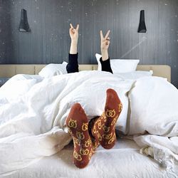 Low section of woman gesturing peace sign while relaxing on bed at home