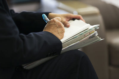 Cropped image of man writing on paper while sitting