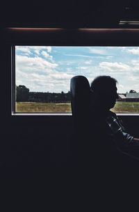 Close-up of man sitting by window against sky