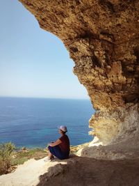 Man sitting on rock looking at sea