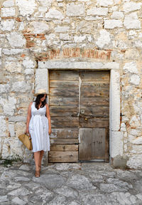 Young woman standing by old wooden door, white dress, summer, lifestyle.