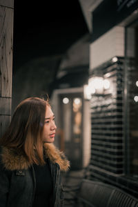 Woman looking away while standing in city at night