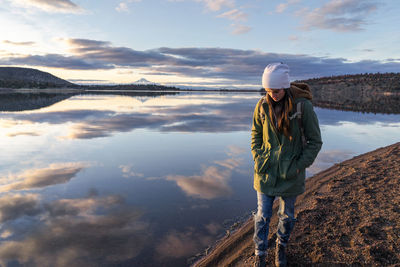 Young woman walking along lake at sunset with mountain in background