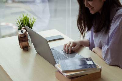 Midsection of woman using smart phone while sitting on table