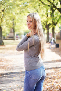 Portrait of smiling teenage girl standing on footpath amidst trees at park