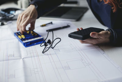 Midsection of female engineer holding portable hard drive on desk