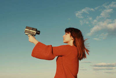 Side view of woman photographing against sky