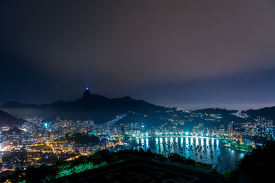 Illuminated cityscape at harbor against sky at night