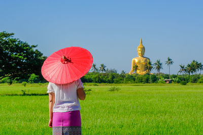 Rear view of woman with umbrella standing in farm against clear sky