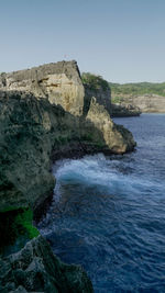 Rock formations by sea against clear blue sky