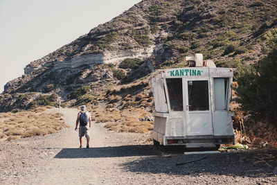 Rear view of man walking on dirt road by mountain