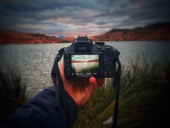 Man photographing camera on sea against sky during sunset