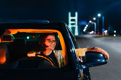 Portrait of man sitting in illuminated car on road at night