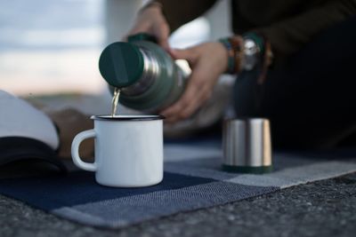 Cropped hands pouring drink in cup on retaining wall