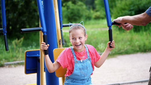 Smiling, happy eight year old girl engaged, doing exercises on outdoor exercise equipment