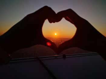 Close-up of silhouette hand holding heart shape against sky during sunset