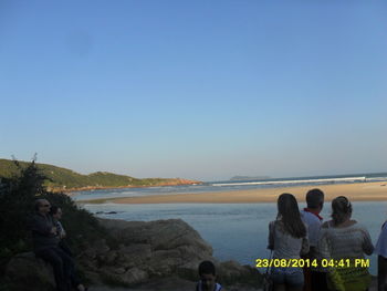 Rear view of people on rocks by sea against clear sky