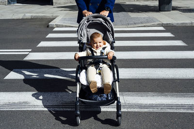 Father with smiling baby in baby stroller crossing road in city