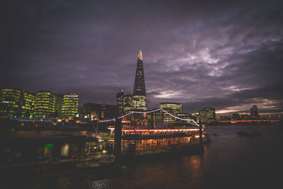 Illuminated city by river against sky at night