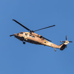 Low angle view of military helicopter flying against clear blue sky