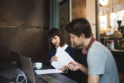 Confident creative colleagues discussing over documents at desk in office