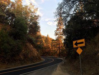 Road sign by trees against sky