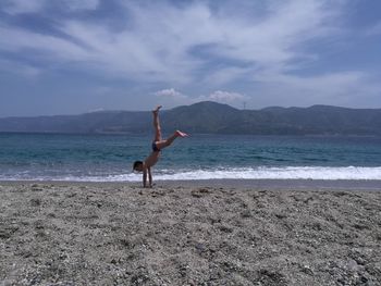 Boy practicing cartwheel at beach against sky