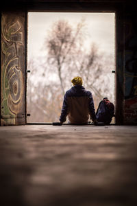 Rear view of boy with backpack sitting on old home entrance