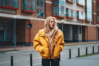 Young woman with hands in pockets standing against building in city