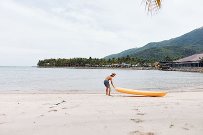 Rear view of woman standing at beach against sky