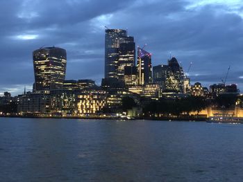 Illuminated buildings by river against sky