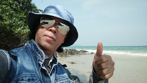 Man showing thumbs up sign at beach against sky