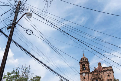 Low angle view of power lines and building against sky