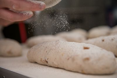 Cropped hand of woman sprinkling flour on bread dough at table